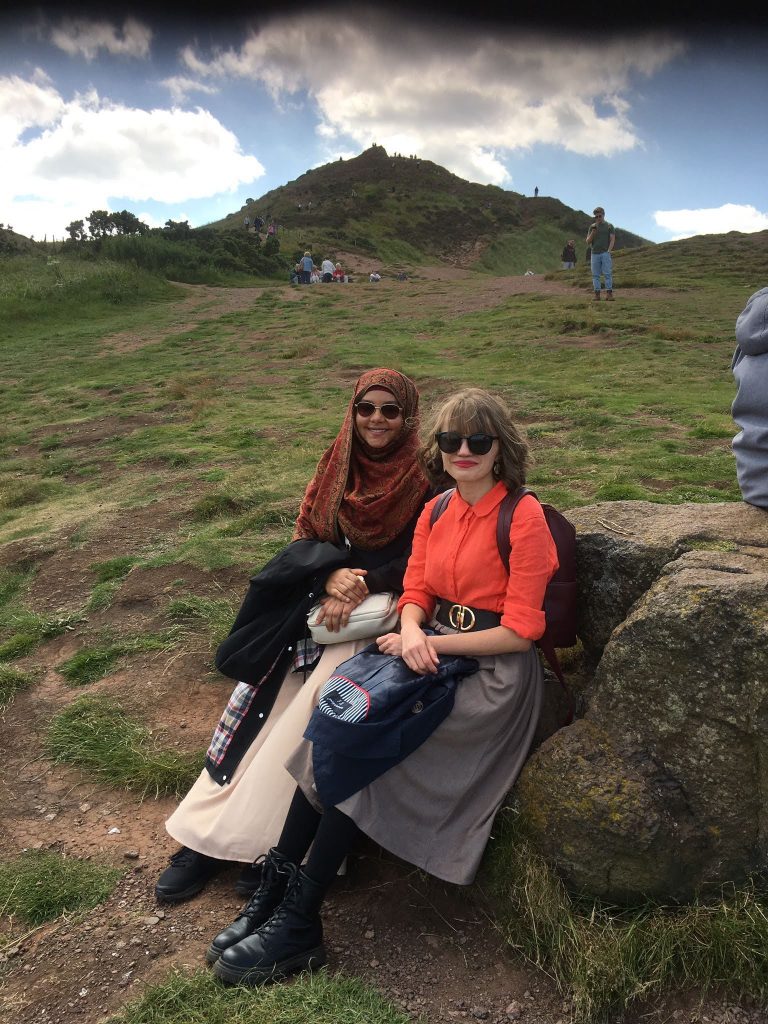 Two women sitting on Arthur's Seat in Edinburgh smiling at the camera.