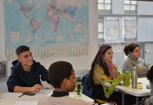 People from different multicultural backgrounds in an English classroom at The Welcoming Association listening to the teacher.